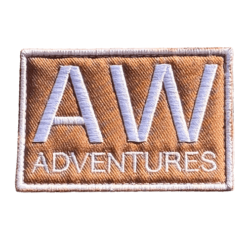 AWA Title embroidered travel patch featuring large white AW lettering above Adventures text on a tan rectangular background.