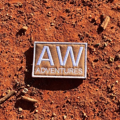 AWA Title embroidered travel patch featuring large white AW lettering above Adventures text on a tan rectangular background.
