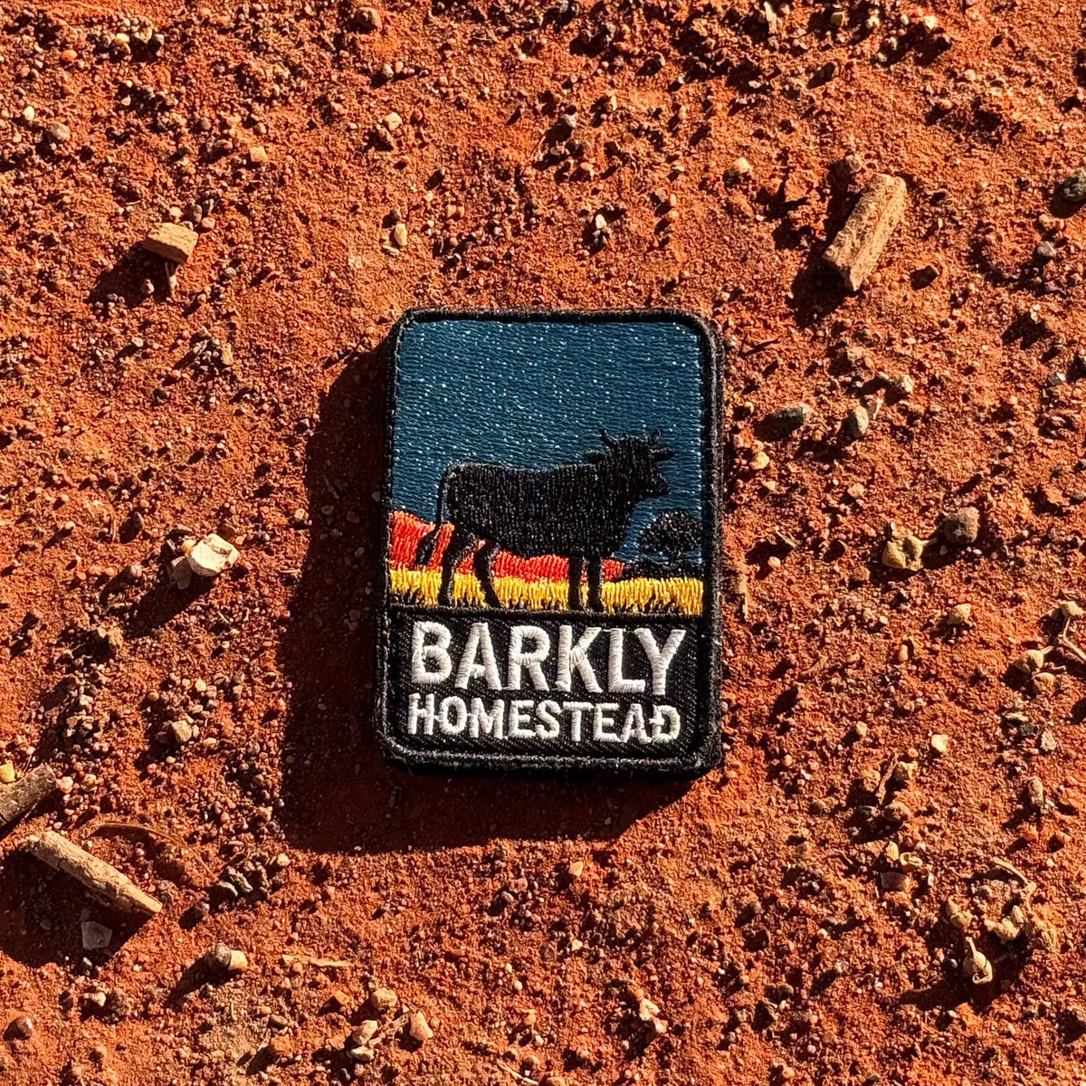 Barkly Homestead embroidered travel patch featuring dark cattle silhouette against orange outback hills and a teal sky.