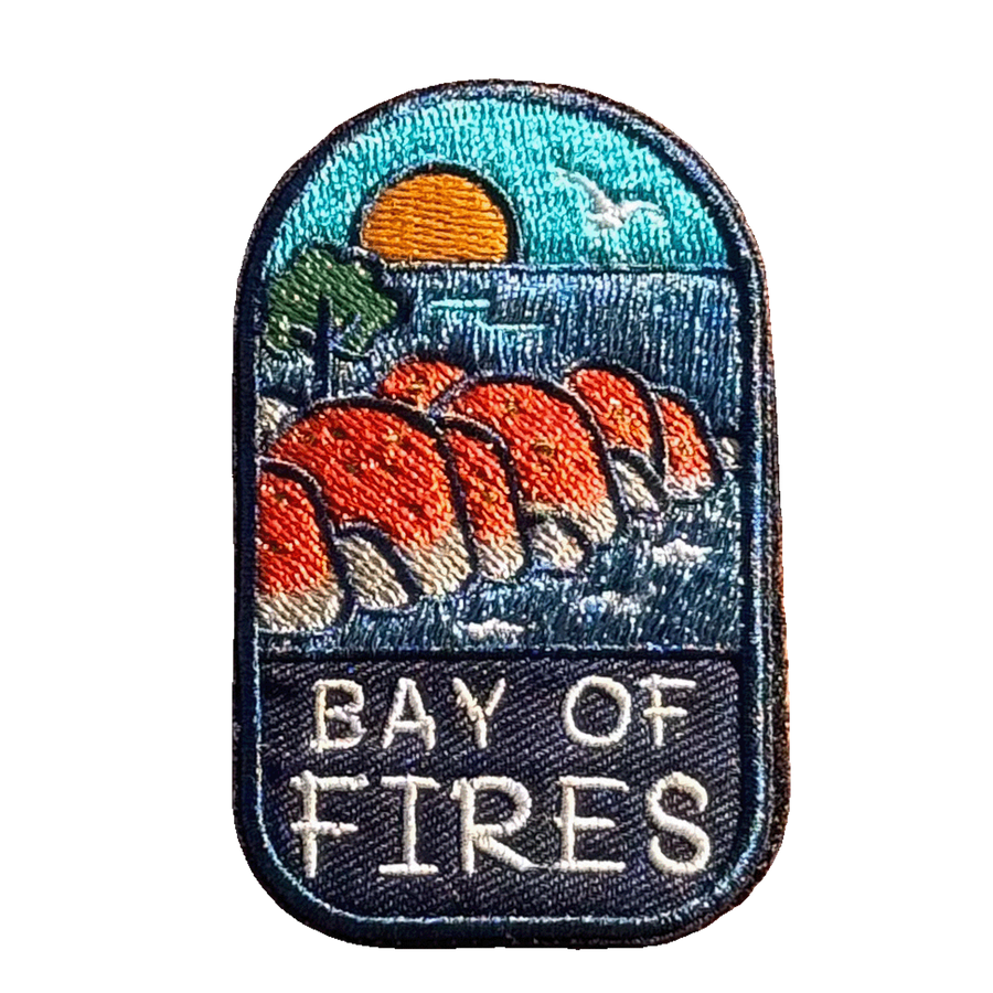 Bay of Fires embroidered travel patch featuring orange coastal boulders, turquoise ocean, a setting sun and a flying seabird.