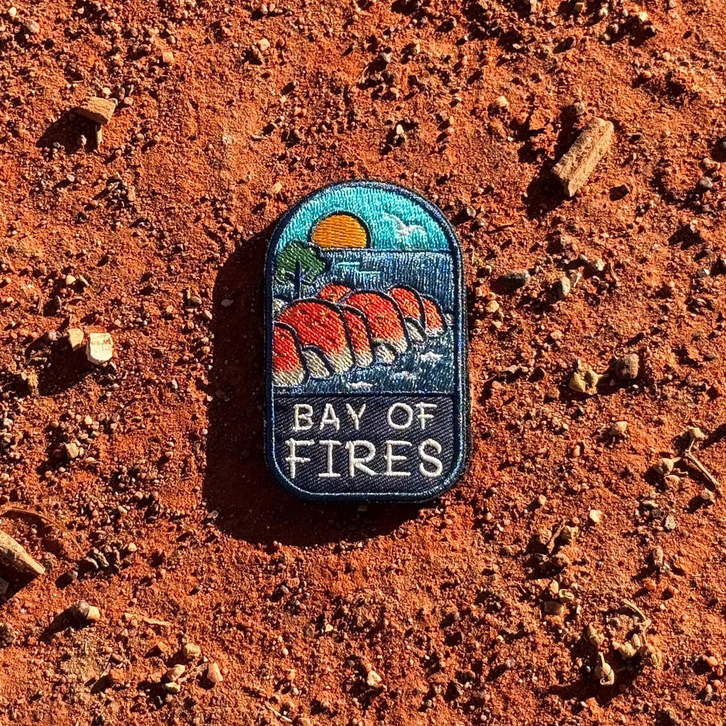 Bay of Fires embroidered travel patch featuring orange coastal boulders, turquoise ocean, a setting sun and a flying seabird.