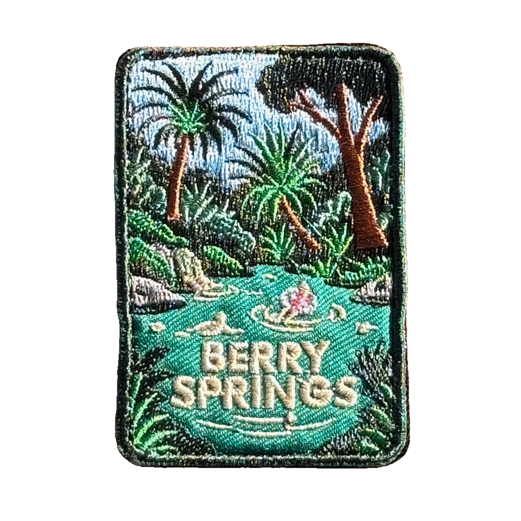 Berry Springs embroidered travel patch featuring swimmers in turquoise water beside a waterfall and lush tropical palms.