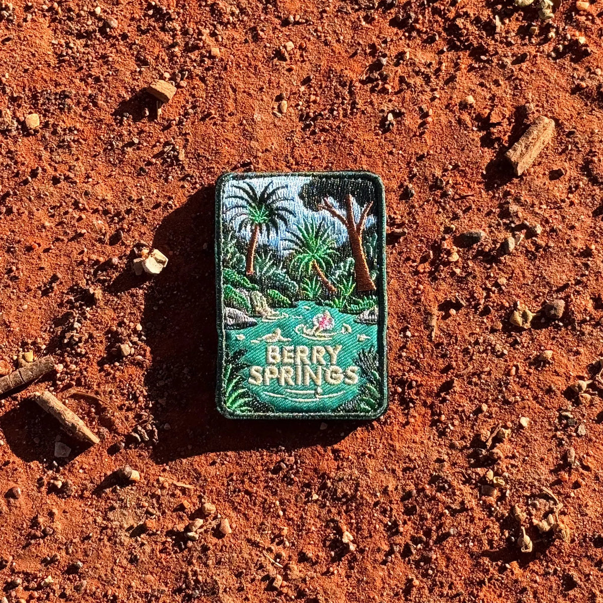 Berry Springs embroidered travel patch featuring swimmers in turquoise water beside a waterfall and lush tropical palms.