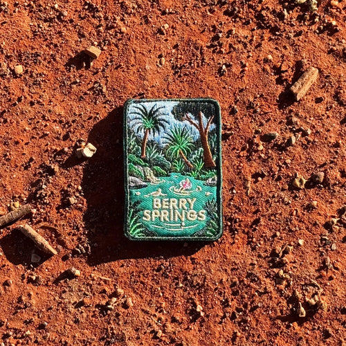 Berry Springs embroidered travel patch featuring swimmers in turquoise water beside a waterfall and lush tropical palms.