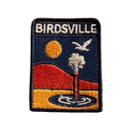Birdsville embroidered travel patch featuring artesian bore releasing water against orange desert dunes, a golden sun and a flying bird.
