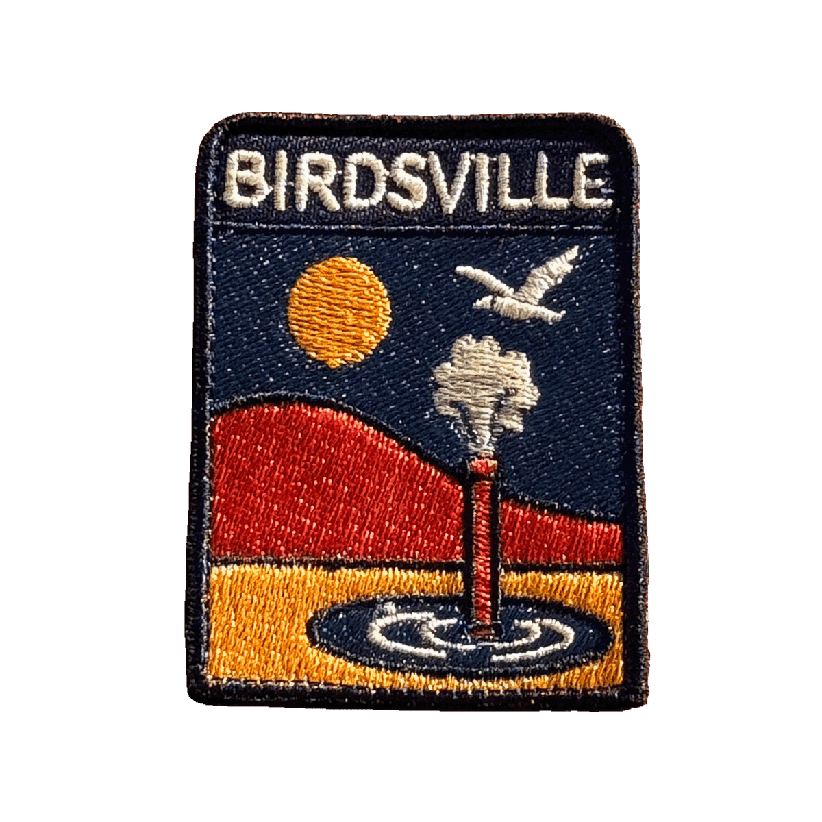Birdsville embroidered travel patch featuring artesian bore releasing water against orange desert dunes, a golden sun and a flying bird.