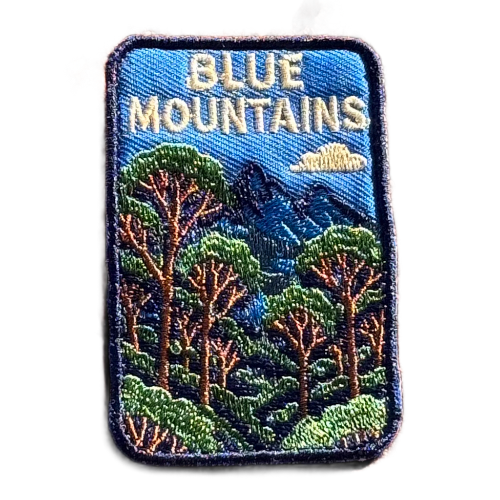 Blue Mountains embroidered travel patch featuring eucalyptus forest, layered blue mountain peaks and a white cloud against a deep blue sky.