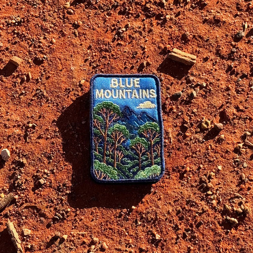 Blue Mountains embroidered travel patch featuring eucalyptus forest, layered blue mountain peaks and a white cloud against a deep blue sky.