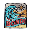 Bondi Beach embroidered travel patch featuring four surfers riding turquoise ocean waves beside a sunny golden beach.