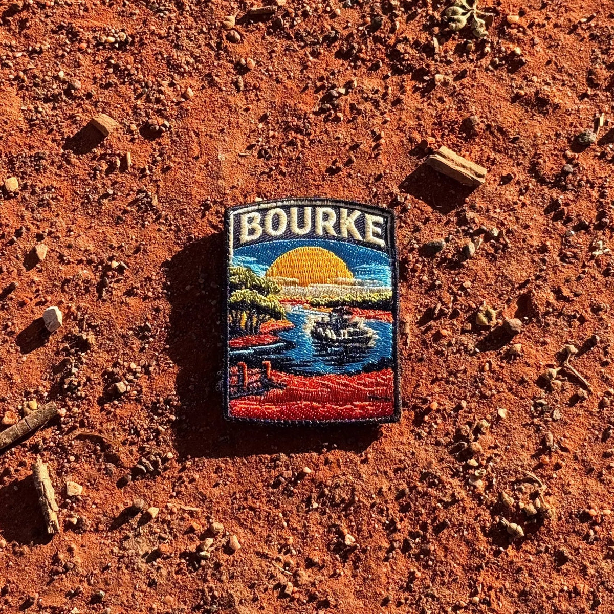 Bourke embroidered travel patch featuring paddle steamer cruising along a winding river through red outback scenery at sunset.