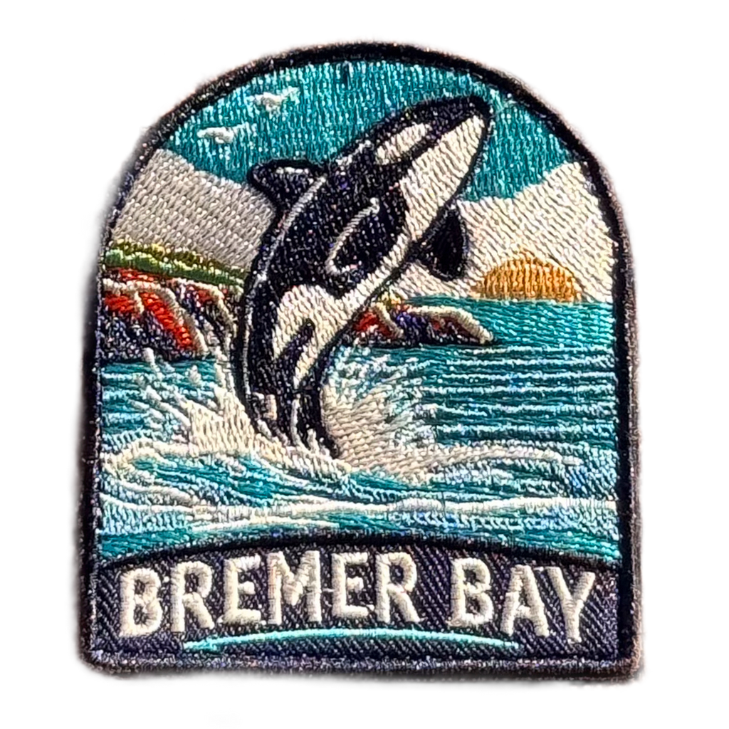 Bremer Bay embroidered travel patch featuring breaching orca splashing in the ocean near a rocky coastline at sunset.