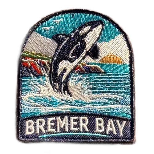 Bremer Bay embroidered travel patch featuring breaching orca splashing in the ocean near a rocky coastline at sunset.