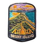 Bruny Island embroidered travel patch with a white lighthouse overlooking a rugged island coast; photographed on a transparent background.