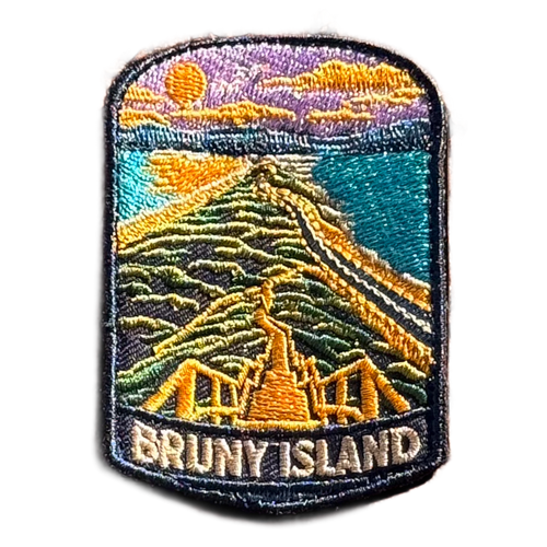 Bruny Island embroidered travel patch with a white lighthouse overlooking a rugged island coast; photographed on a transparent background.