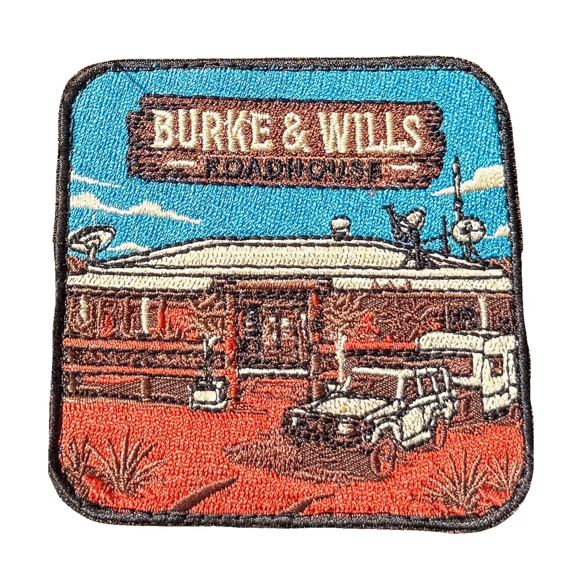 Burke And Wills Roadhouse embroidered travel patch with a remote roadhouse in red outback country; photographed on a transparent background.