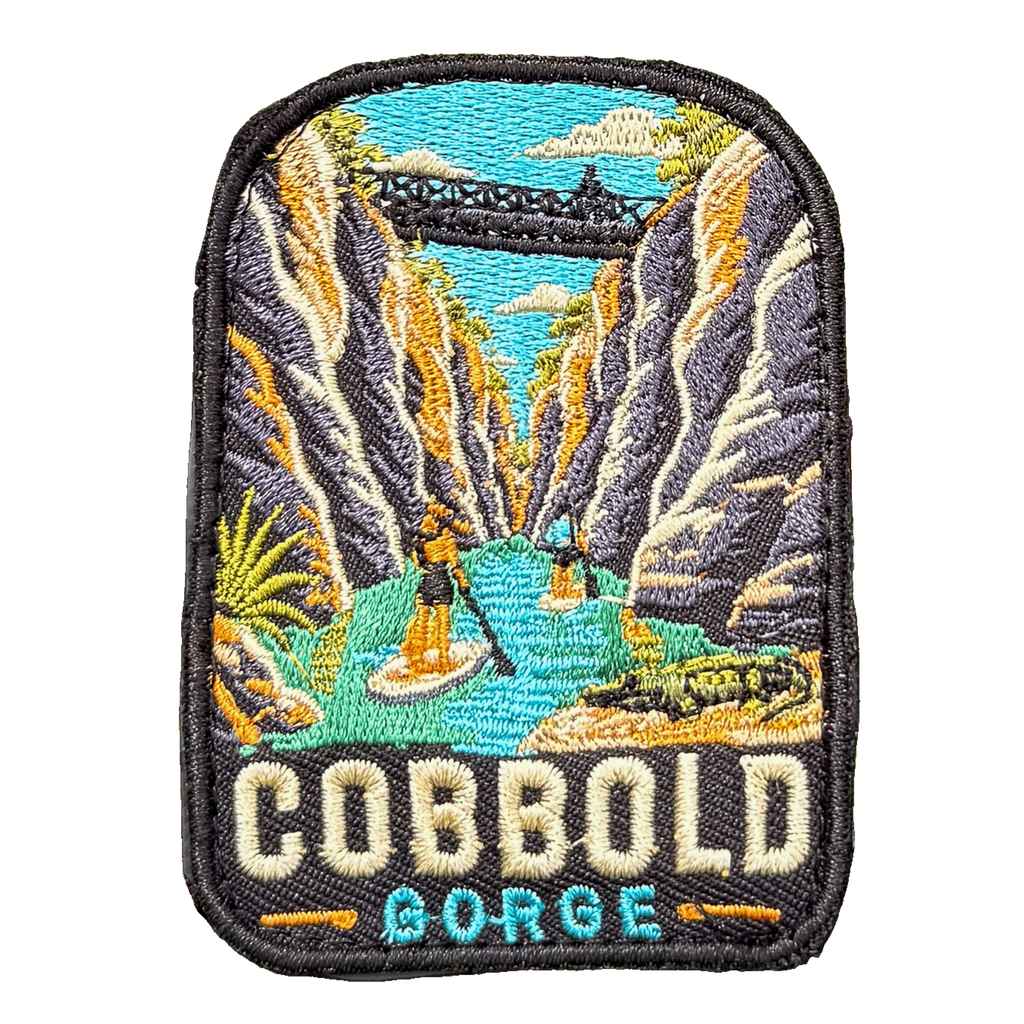 Cobbold Gorge embroidered travel patch with a boat travelling between narrow sandstone gorge walls; photographed on a transparent background.