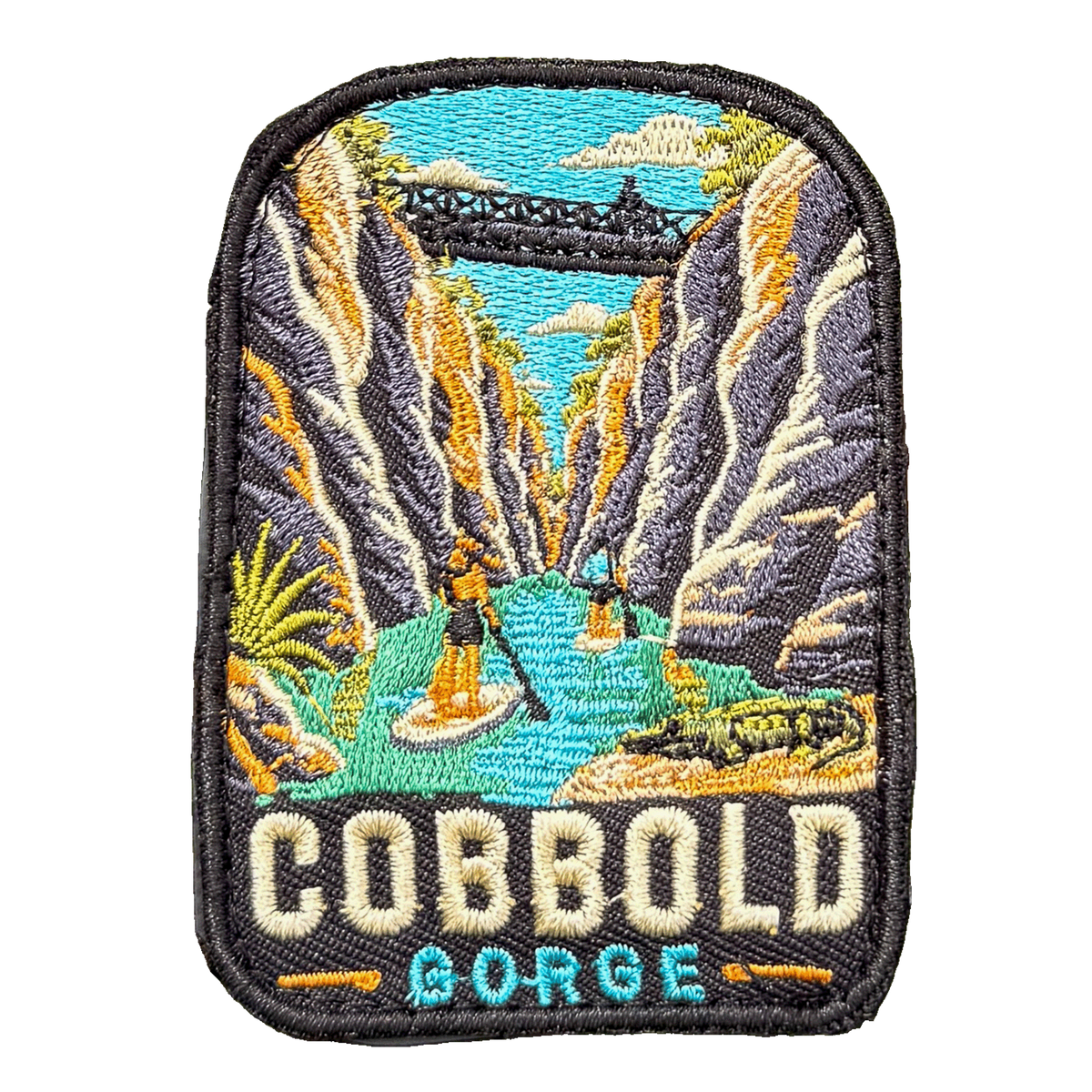 Cobbold Gorge embroidered travel patch with a boat travelling between narrow sandstone gorge walls; photographed on a transparent background.