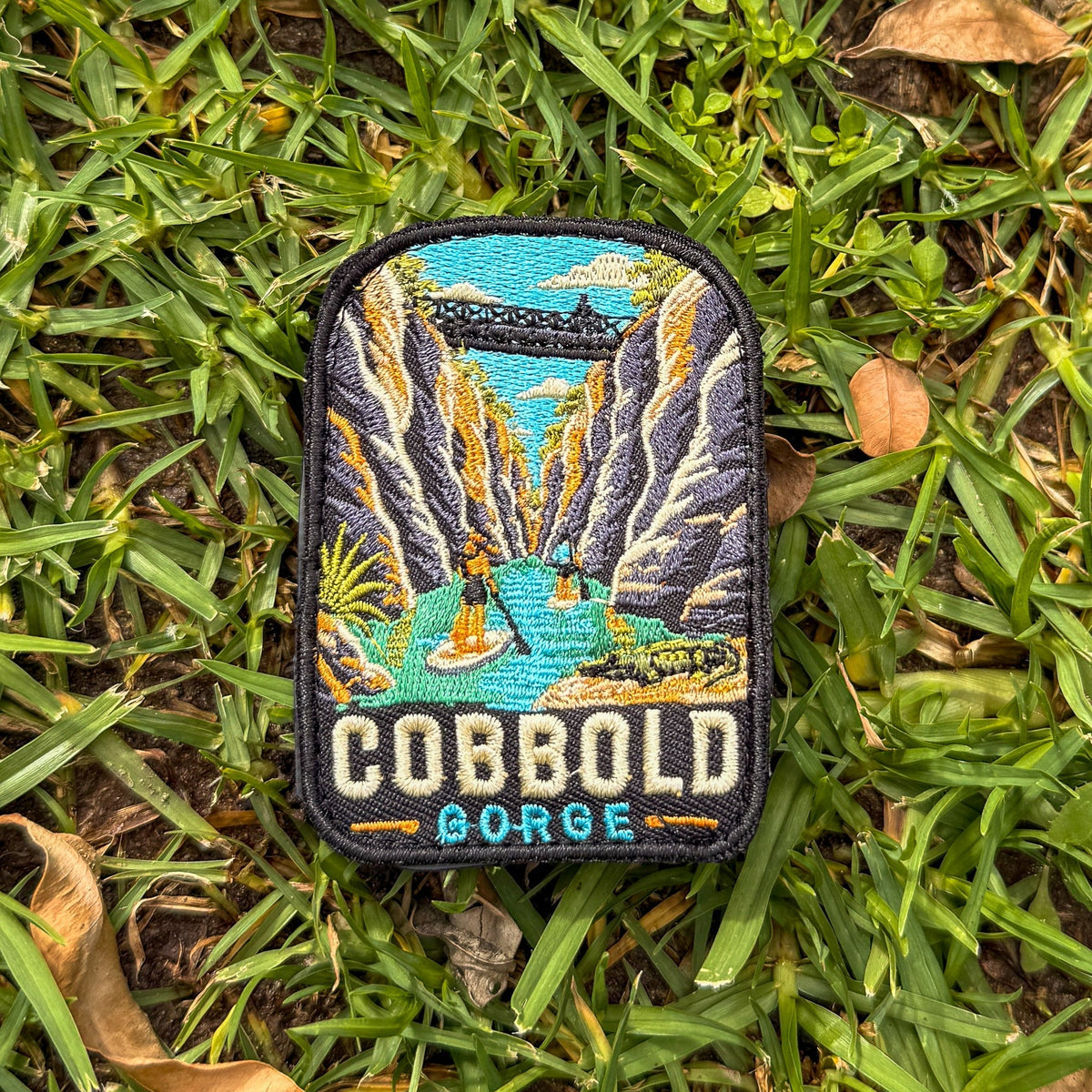 Cobbold Gorge embroidered travel patch with a boat travelling between narrow sandstone gorge walls.