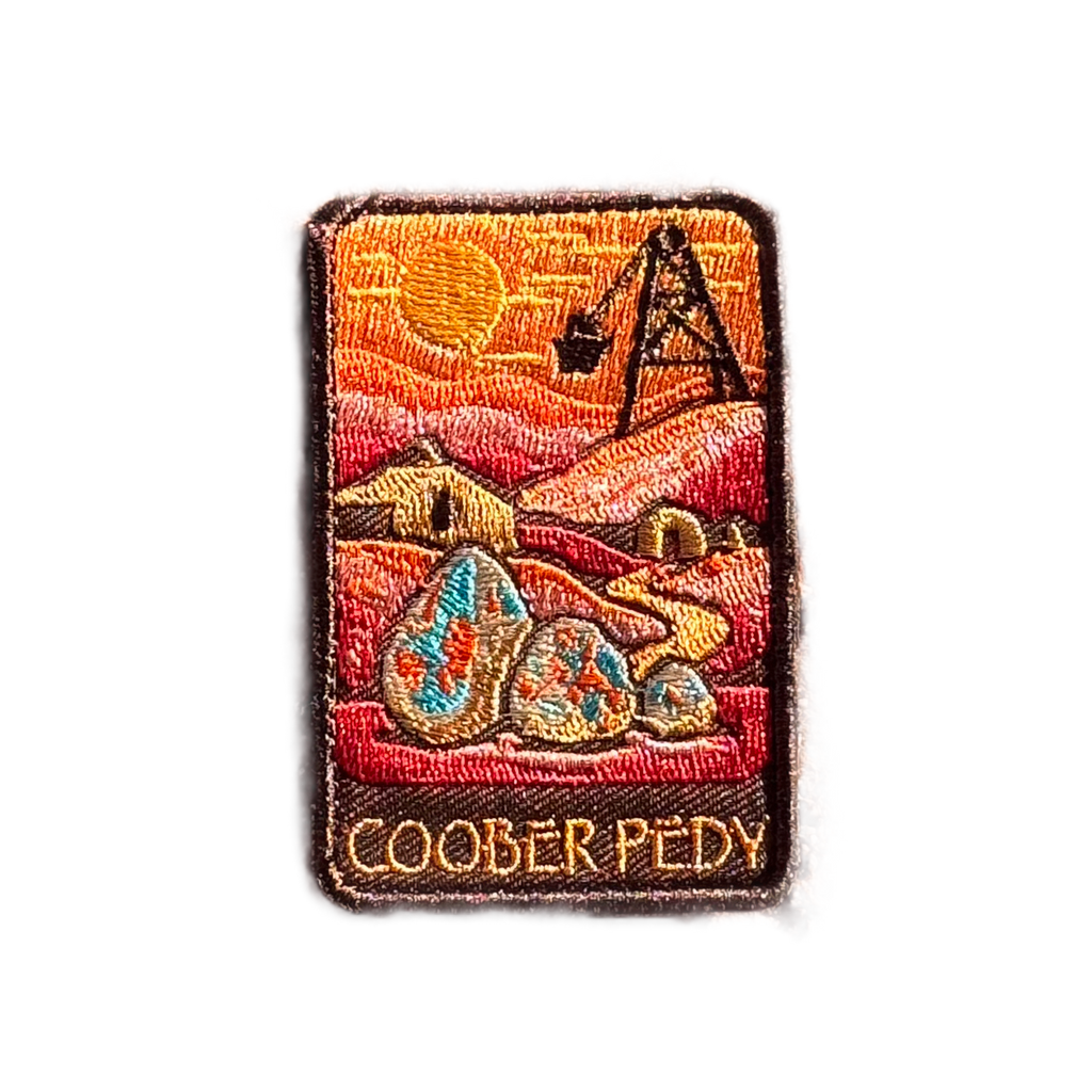 Coober Pedy embroidered travel patch with an opal-mining and underground dugout landscape; photographed on a transparent background.