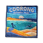 Coorong National Park embroidered travel patch with a pelican on sand dunes and a dolphin in turquoise coastal water; photographed on a transparent background.