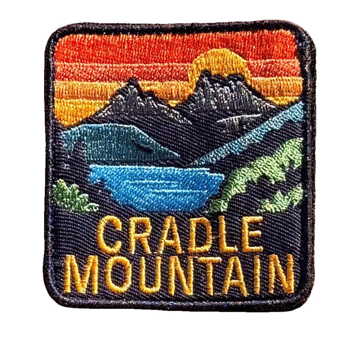 Cradle Mountain embroidered travel patch with Cradle Mountain peaks reflected in a blue lake at sunset; photographed on a transparent background.