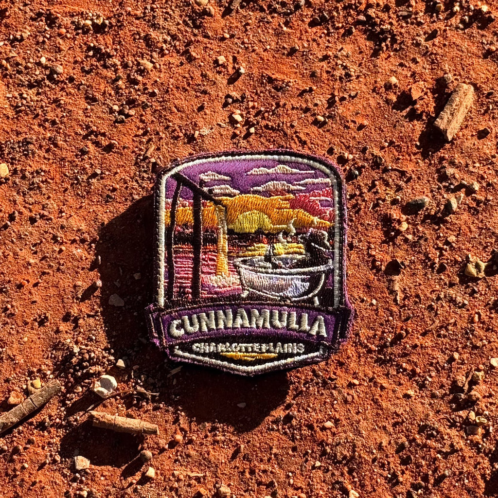 Cunnamulla - Charlotte Plains embroidered travel patch with a person relaxing in an outdoor bath at Charlotte Plains beneath a sunset sky.