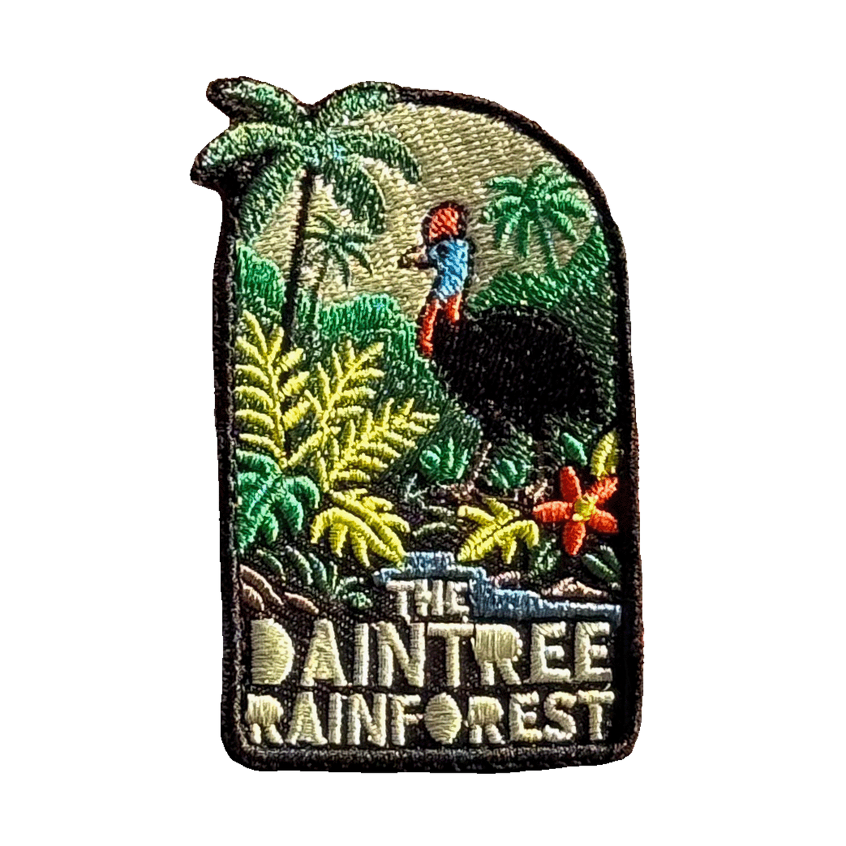 Daintree Rainforest embroidered travel patch with a cassowary surrounded by tropical rainforest, palms and flowers; photographed on a transparent background.