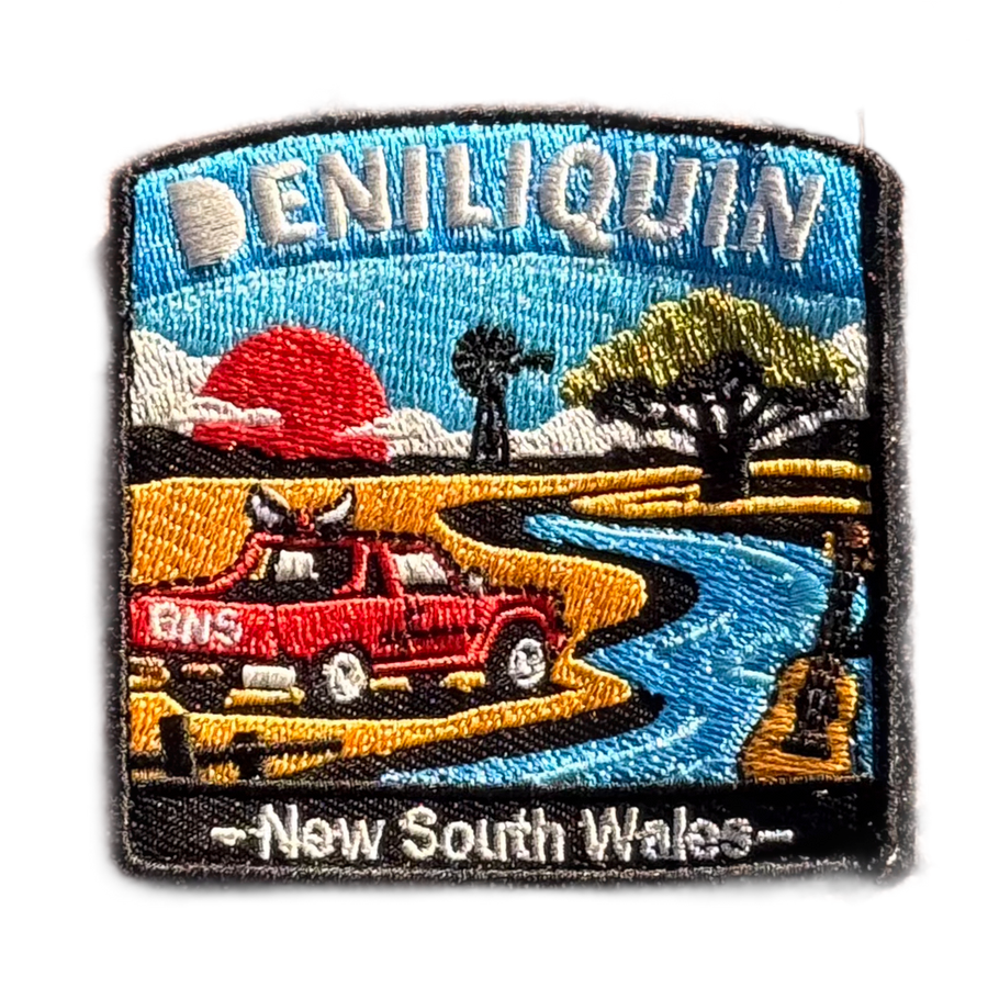 Deniliquin embroidered travel patch with a red ute, guitar, windmill and winding river beneath an orange sunset; photographed on a transparent background.