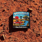 Deniliquin embroidered travel patch with a red ute, guitar, windmill and winding river beneath an orange sunset.