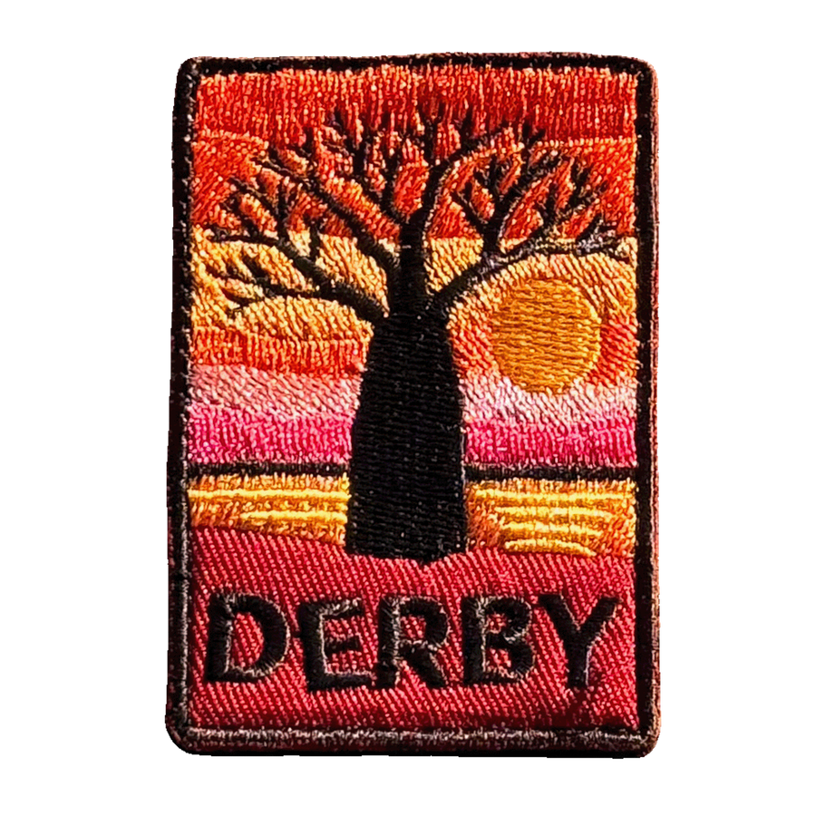 Derby embroidered travel patch with a jetty extending across tidal flats at sunset; photographed on a transparent background.
