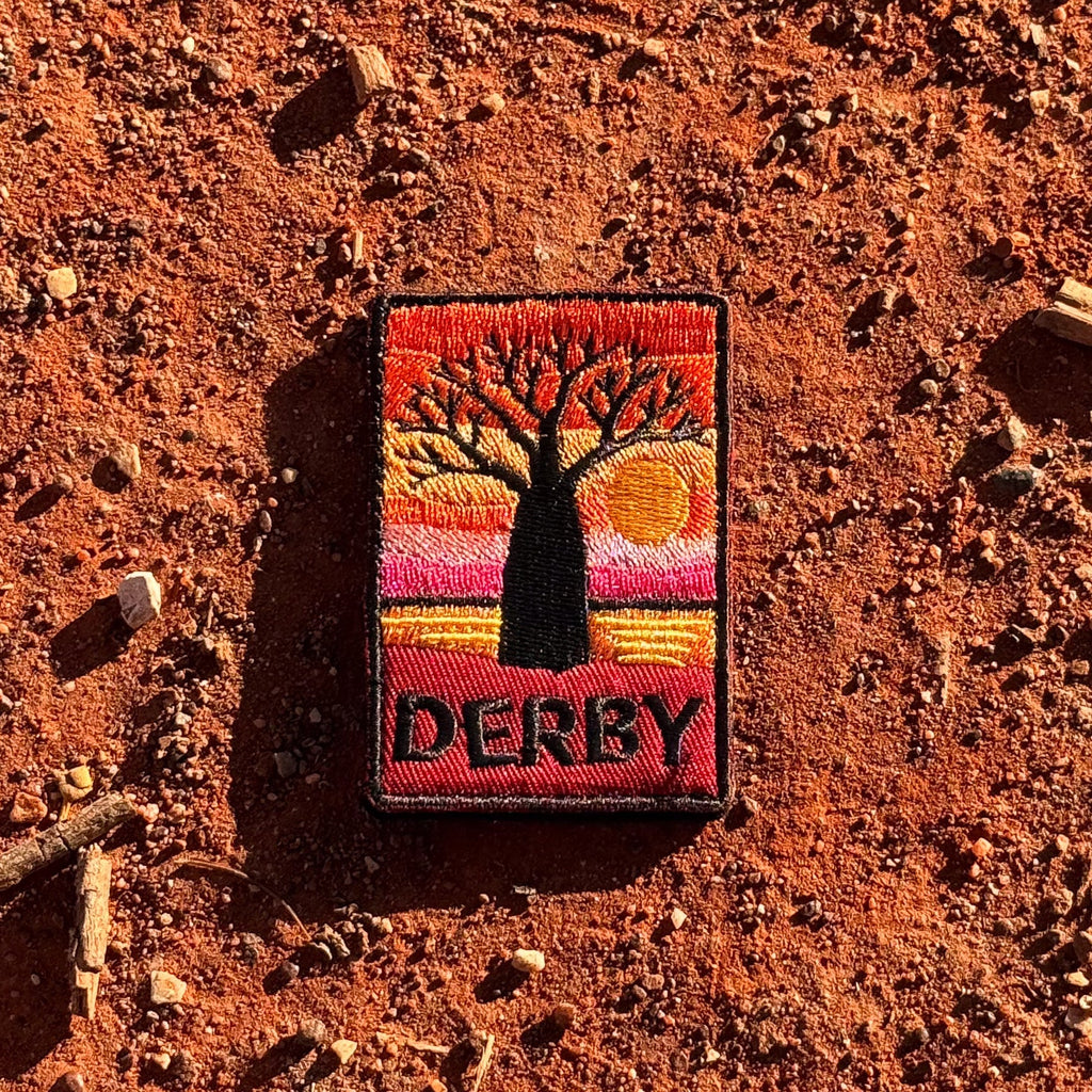Derby embroidered travel patch with a jetty extending across tidal flats at sunset.