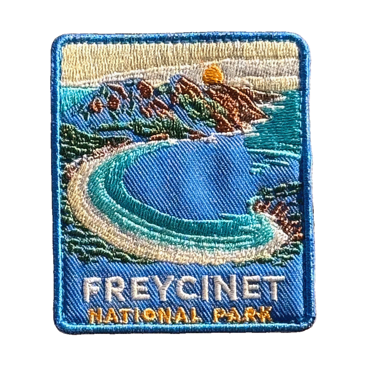 Freycinet - Wineglass Bay embroidered travel patch with Wineglass Bay, turquoise water and granite mountains; photographed on a transparent background.