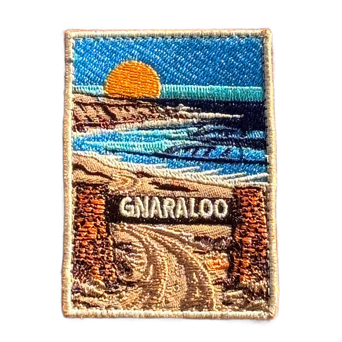 Gnaraloo Station embroidered travel patch with a breaking ocean wave along a rugged coastline; photographed on a transparent background.