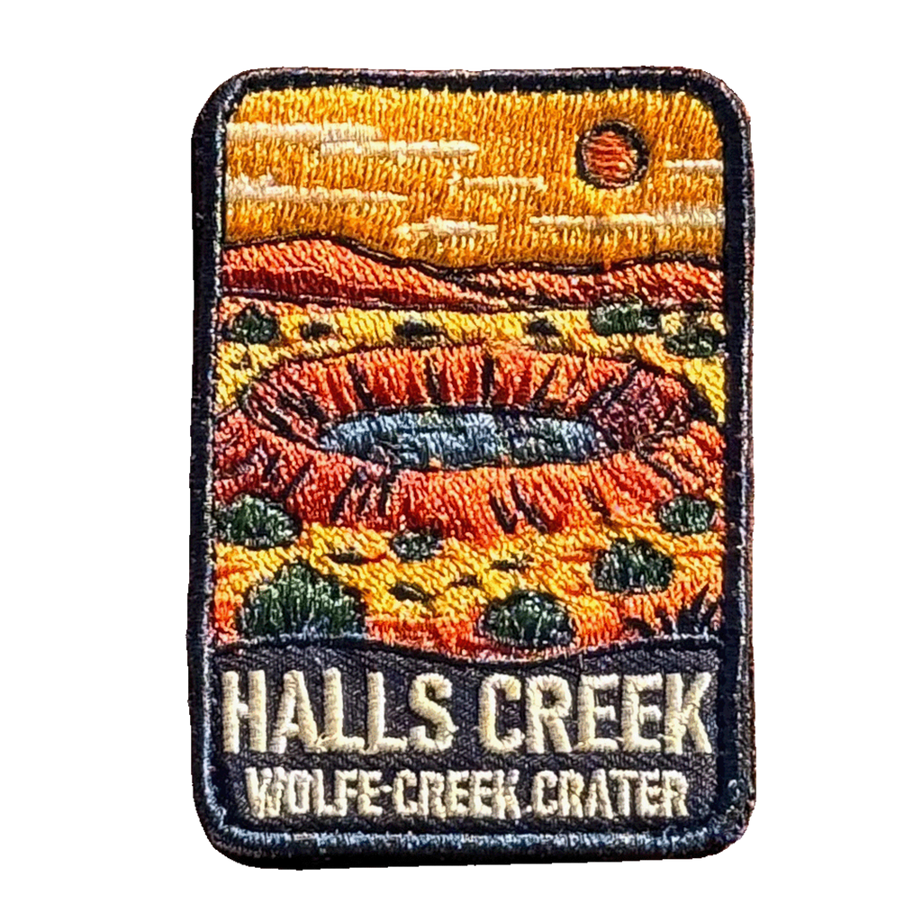 Halls Creek - Wolfe Creek Crater embroidered travel patch with the circular Wolfe Creek Crater in a red desert landscape; photographed on a transparent background.