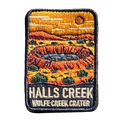 Halls Creek - Wolfe Creek Crater embroidered travel patch with the circular Wolfe Creek Crater in a red desert landscape; photographed on a transparent background.