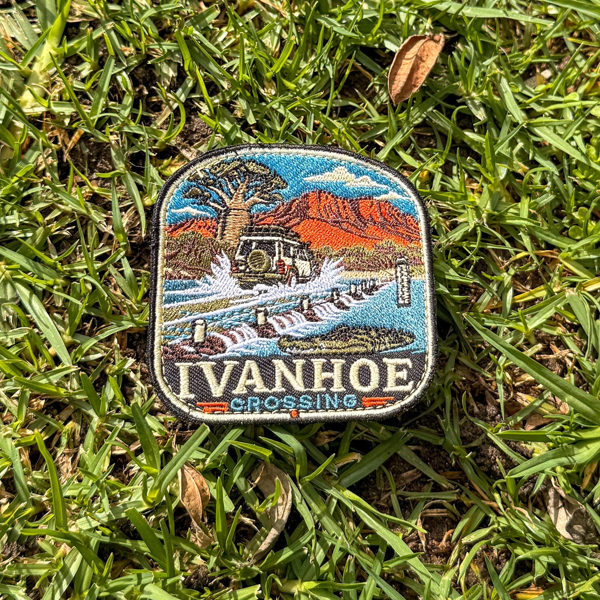 Ivanhoe Crossing embroidered travel patch with a four-wheel drive splashing across a flooded causeway with a crocodile in the water.