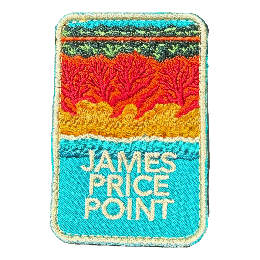James Price Point embroidered travel patch with layered red coastal cliffs, turquoise water and a dark green treeline; photographed on a transparent background.