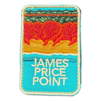 James Price Point embroidered travel patch with layered red coastal cliffs, turquoise water and a dark green treeline; photographed on a transparent background.