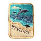 Jervis Bay embroidered travel patch with dolphins leaping offshore and a turtle swimming beside a sandy beach; photographed on a transparent background.