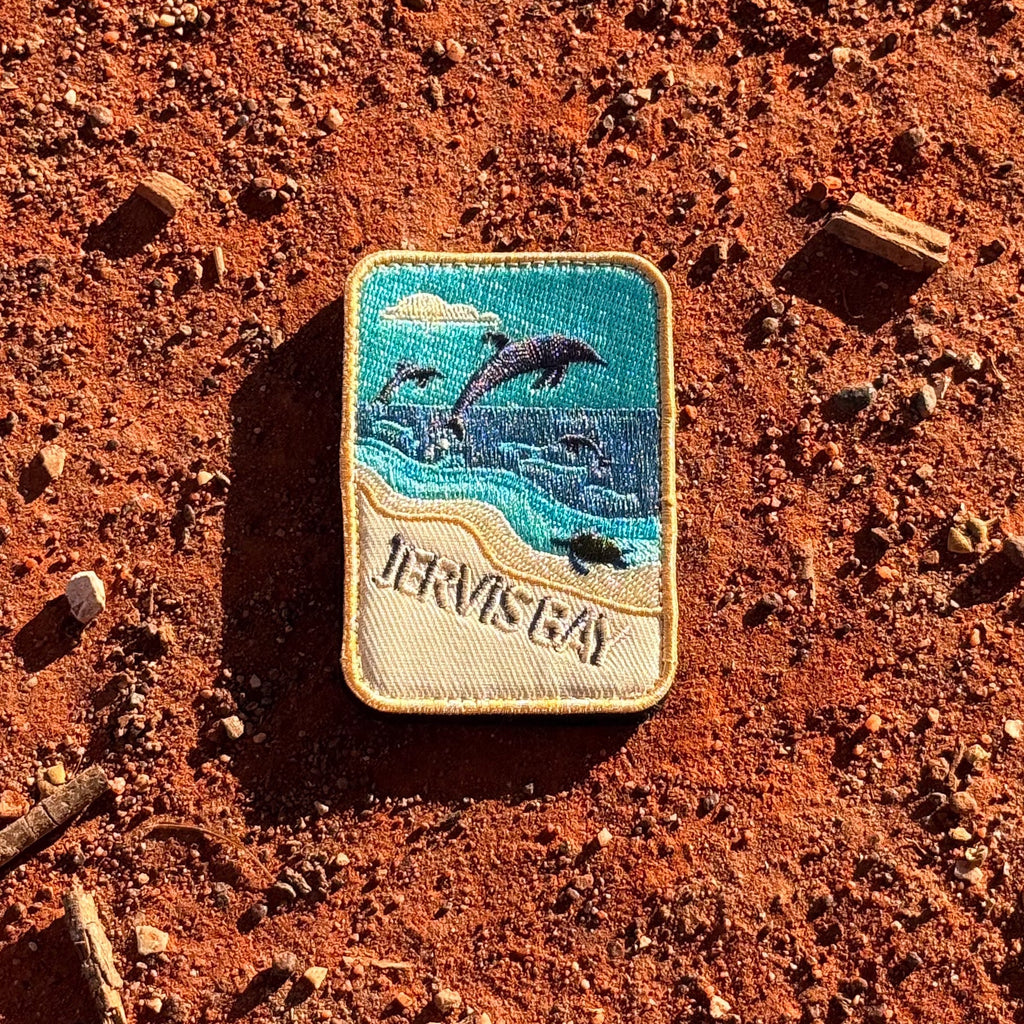 Jervis Bay embroidered travel patch with dolphins leaping offshore and a turtle swimming beside a sandy beach.