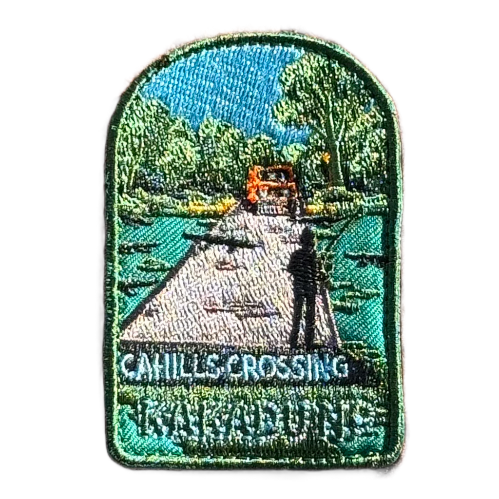 Kakadu - Cahills Crossing embroidered travel patch with a four-wheel drive approaching a river crossing in Kakadu, with trees and a person fishing; photographed on a transparent background.