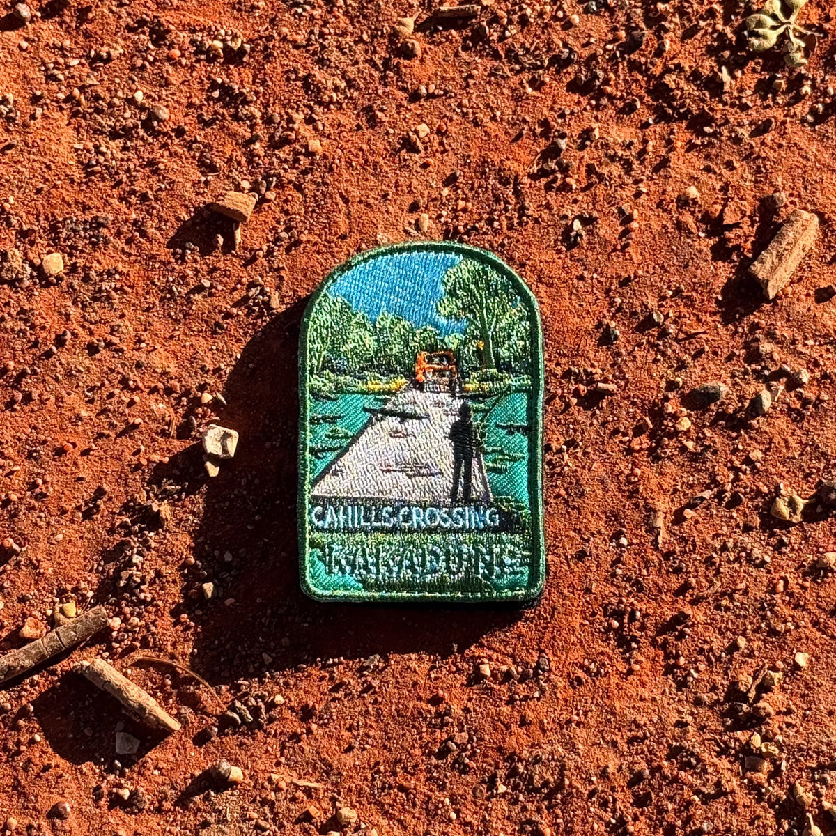 Kakadu - Cahills Crossing embroidered travel patch with a four-wheel drive approaching a river crossing in Kakadu, with trees and a person fishing.