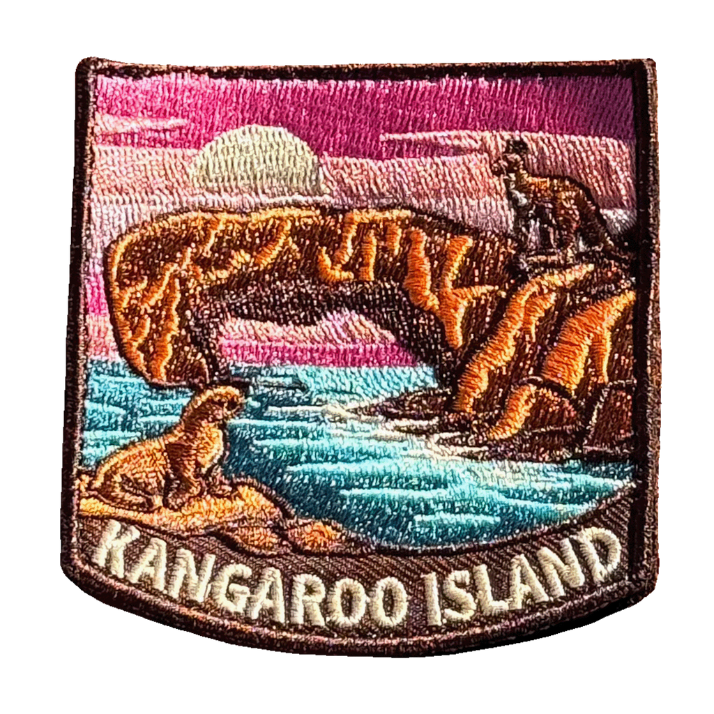 Kangaroo Island embroidered travel patch with a kangaroo on a coastal rock arch and a sea lion beside turquoise water at sunset; photographed on a transparent background.