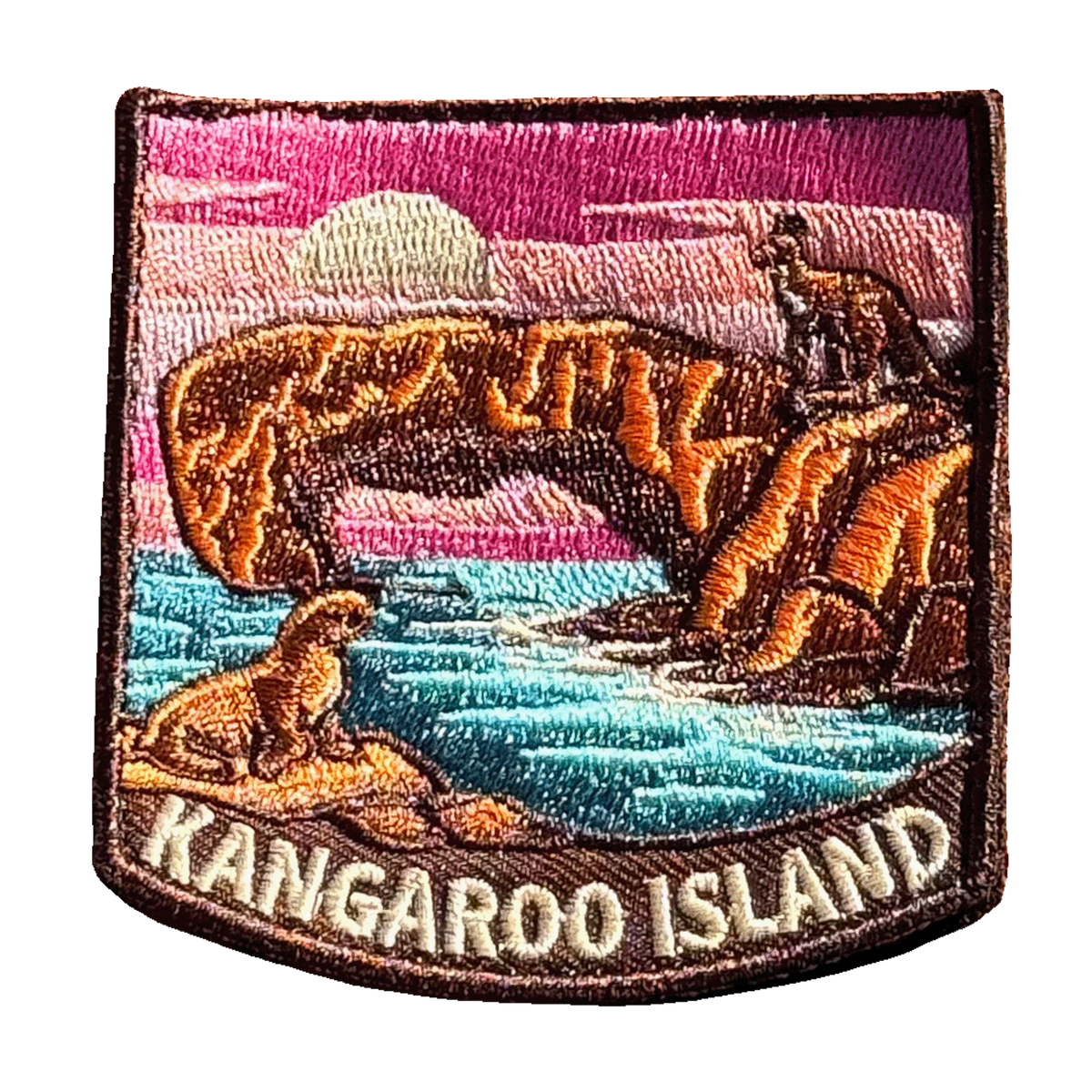 Kangaroo Island embroidered travel patch with a kangaroo on a coastal rock arch and a sea lion beside turquoise water at sunset; photographed on a transparent background.
