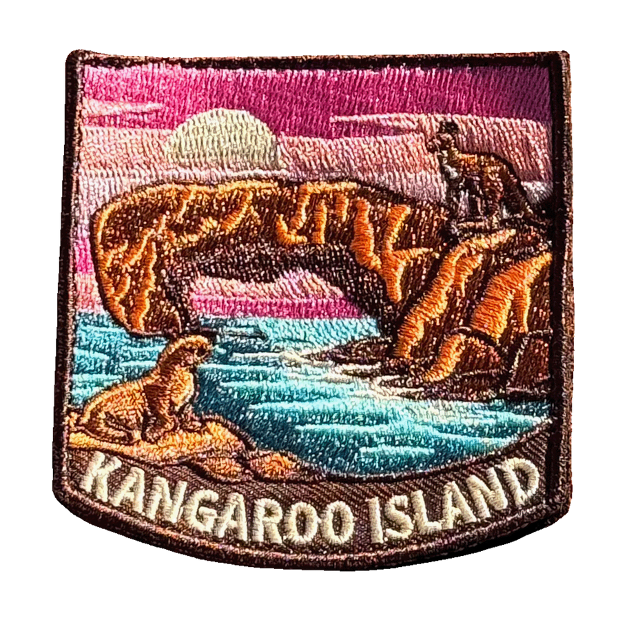 Kangaroo Island embroidered travel patch with a kangaroo on a coastal rock arch and a sea lion beside turquoise water at sunset; photographed on a transparent background.