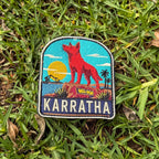 Karratha embroidered travel patch with the Red Dog statue on a red rocky hill with an industrial harbour and sunset.
