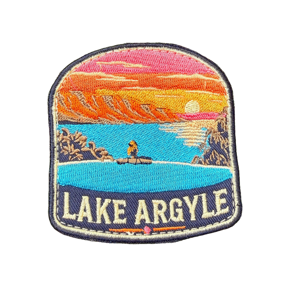 Lake Argyle embroidered travel patch with a swimmer overlooking Lake Argyle and distant mountains at sunset; photographed on a transparent background.