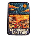 Lake Eyre (Kati Thanda) embroidered travel patch with cracked salt flats and shallow water beneath an orange sun at Kati Thanda‚ÄìLake Eyre; photographed on a transparent background.