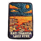 Lake Eyre (Kati Thanda) embroidered travel patch with cracked salt flats and shallow water beneath an orange sun at Kati Thanda‚ÄìLake Eyre; photographed on a transparent background.