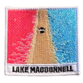 Lake MacDonnell embroidered travel patch with an aerial view of a road separating bright pink and blue lakes; photographed on a transparent background.